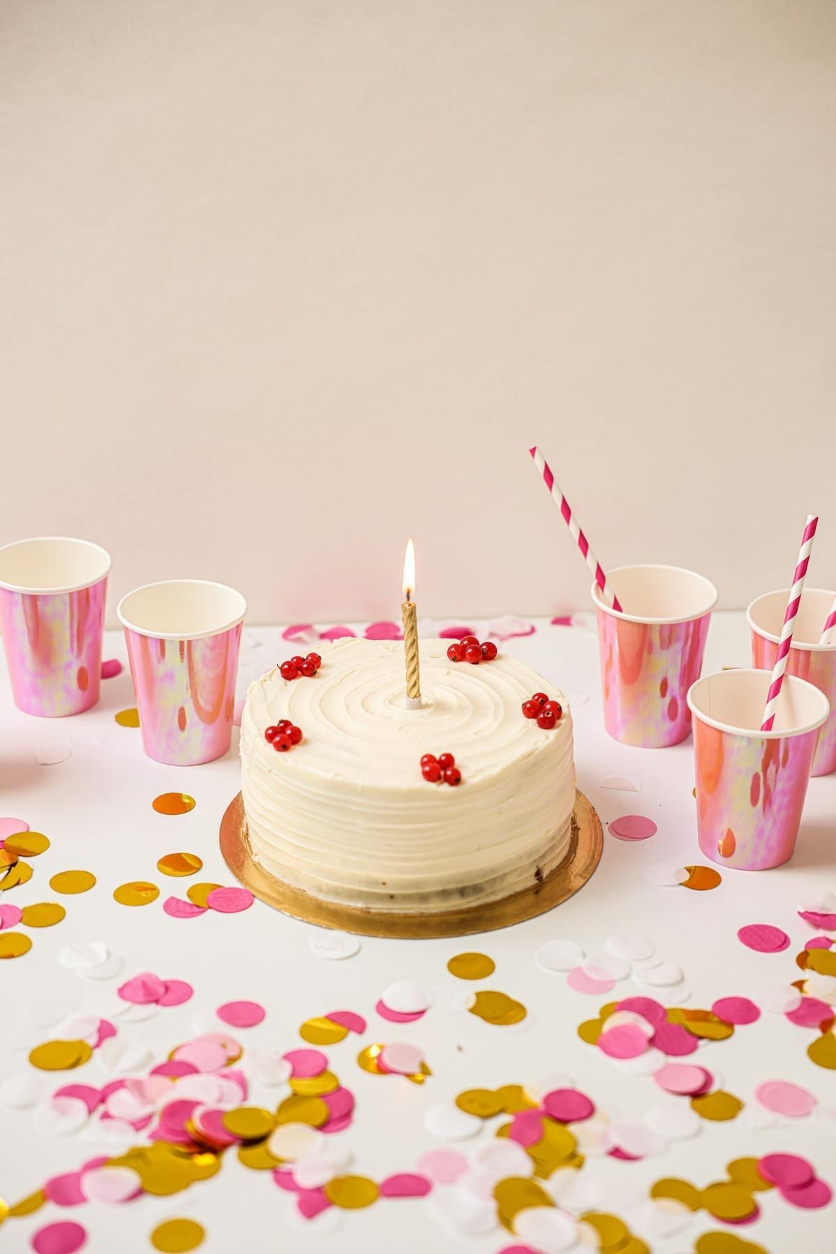 Birthday cake with a lit candle surrounded by colorful cups and confetti