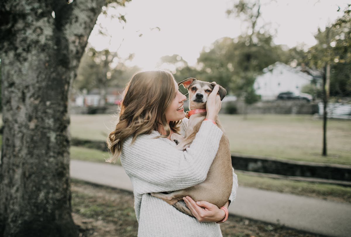 Smiling woman hugging her dog outdoors in a sunny park